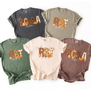 May include: Five different colored t-shirts with fall-themed designs. Each shirt features a name and the letters RBT or BCBA in a fall leaf pattern, with pumpkins and a coffee cup graphic. The shirts are in various colors.