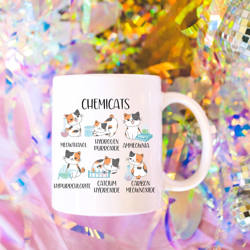 K&ouml;nnte beinhalten: Eine wei&szlig;e Keramiktasse mit einer Schwarzwei&szlig;illustration von Katzen mit chemischen Formeln. Der Text "CHEMICATS" befindet sich oben auf der Tasse. Die Katzenillustrationen sind mit den folgenden chemischen Formeln beschriftet: "MEOUTHANOL", "HYDROGEN PURROXIDE", "AMMEOWNIA", "HYPURRCHLORITE", "CATCIUM HYDROXIDE" und "CARBON MEOANNOXIDE".