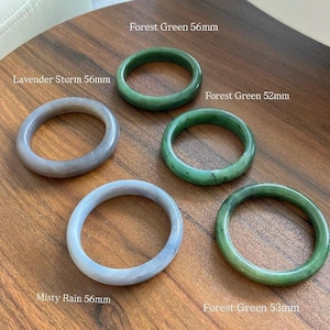 Pode incluir: Cinco pulseiras circulares lisas de várias cores e tamanhos. Duas são cinza-lavanda rotuladas como Lavender Storm 56mm e Misty Rain 56mm. Três são verdes rotuladas como Forest Green 56mm, Forest Green 52mm e Forest Green 53mm.
