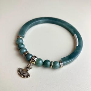 May include: A dark green jade bangle bracelet featuring a segment of round jade beads interspersed with silver-toned metal spacers. A silver-toned metal fan-shaped charm hangs from the center of the bead section, which is attached to the solid jade band.