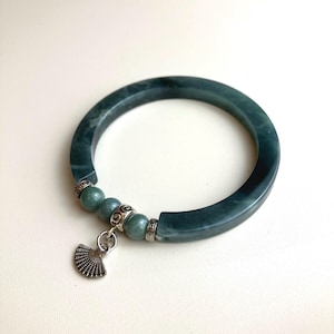 May include: A dark green jade bangle bracelet featuring a segment of three smaller jade beads separated by silver-toned metal spacers. A small silver-toned metal fan-shaped charm hangs from the center of the bead section on a circular ring.
