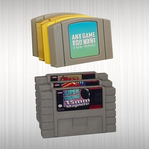 May include: A collection of gray and yellow plastic video game cartridge replicas. The top unit features a blue and green label with the text ANY GAME YOU WANT. The bottom unit displays labels with the text SUPER STRONG 15mm Magnets.
