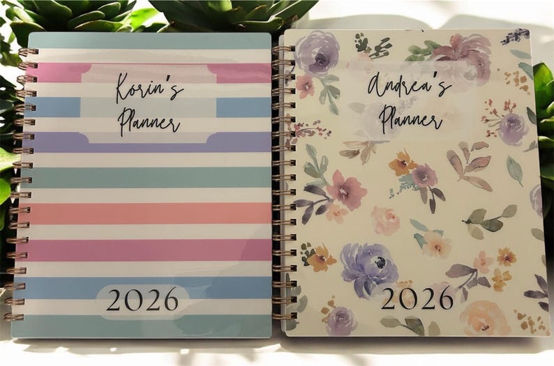 Może przedstawiać: Dwa planery w oprawie spiralnej. Jeden ma wz&oacute;r w paski w pastelowych kolorach z napisem "Korin's Planner" i "2026". Drugi ma kwiatowy wz&oacute;r z napisem "Andrea's Planner" i "2026".