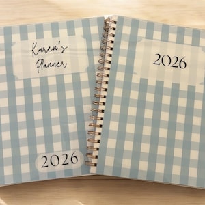 Może przedstawiać: Dwa otwarte planery w oprawie spiralnej z jasnoniebieskimi i białymi okładkami w kratę vichy. Jeden planer zawiera napis "Karen's Planner" i "2026". Drugi planer zawiera napis "2026". Planery są otwarte, ukazując spiralną oprawę i wz&oacute;r okładki.