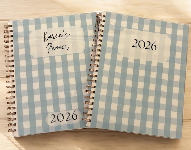 Może przedstawiać: Dwa otwarte planery w oprawie spiralnej z jasnoniebieskimi i białymi okładkami w kratę vichy. Jeden planer zawiera napis "Karen's Planner" i "2026". Drugi planer zawiera napis "2026". Planery są otwarte, ukazując spiralną oprawę i wz&oacute;r okładki.