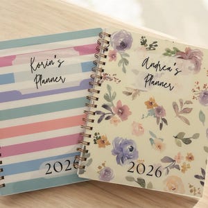 Może przedstawiać: Dwa spiralnie oprawione planery. Jeden ma pastelowy wz&oacute;r w paski z tekstem "Korin's Planner" i "2026". Drugi ma kwiatowy wz&oacute;r z tekstem "Andrea's Planner" i "2026".