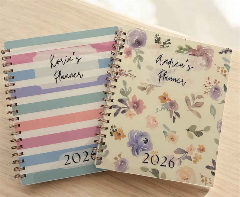 Może przedstawiać: Dwa spiralnie oprawione planery. Jeden ma pastelowy wz&oacute;r w paski z tekstem "Korin's Planner" i "2026". Drugi ma kwiatowy wz&oacute;r z tekstem "Andrea's Planner" i "2026".