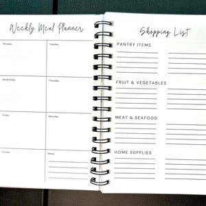 May include: A spiral-bound planner open to two pages. The left page is titled Weekly Meal Planner with sections for Monday through Sunday and a notes area. The right page is titled Shopping List with categories for Pantry Items, Fruit & Vegetables, Meat & Seafood, and Home Supplies.