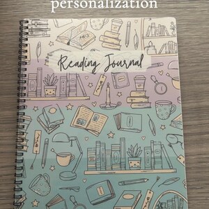 Pode incluir: Um di&aacute;rio de leitura em espiral azul e roxo com um design caprichoso que apresenta livros, x&iacute;caras de caf&eacute;, estrelas e uma vela. A capa diz "Reading Journal".