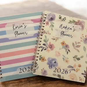 Może przedstawiać: Dwa spiralnie oprawione planery. Jeden ma wz&oacute;r w paski w pastelowych kolorach z nadrukiem "Korin's Planner" i "2026". Drugi ma kwiatowy wz&oacute;r z nadrukiem "Andrea's Planner" i "2026".