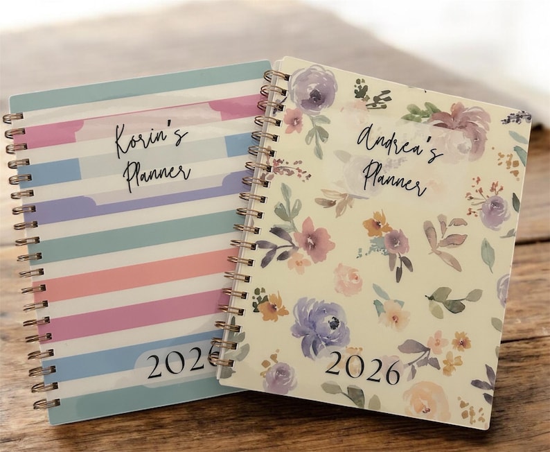 Może przedstawiać: Dwa spiralnie oprawione planery. Jeden ma wz&oacute;r w paski w pastelowych kolorach z nadrukiem "Korin's Planner" i "2026". Drugi ma kwiatowy wz&oacute;r z nadrukiem "Andrea's Planner" i "2026".