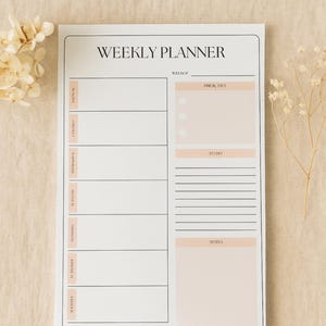 May include: A white weekly planner with a minimalist design. The planner features sections for each day of the week, priorities, to-do lists, and notes. The text "WEEKLY PLANNER" is at the top, with a soft peach color used for accents.