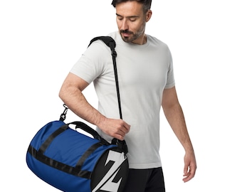 May include: A blue and black duffel bag with a white "Z" logo on the side. The bag has a black shoulder strap and handles. The bag is cylindrical and appears to be made of a durable material.
