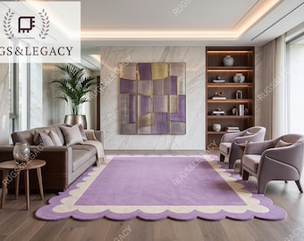 May include: A rectangular area rug featuring a solid lavender center and a wide, cream-colored scalloped border. The rug is positioned on a wooden floor in a room with a brown sofa, two matching armchairs, a wooden side table, and wall art.