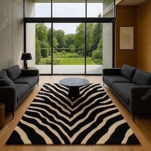Puede incluir: Un salón moderno con una alfombra con estampado de cebra en negro y beige. Dos sofás grises oscuros se enfrentan, con una mesa de centro redonda negra en el centro. Una gran ventana ofrece una vista de un paisaje verde.
