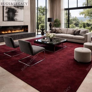 Puede incluir: Salón moderno con una gran alfombra rojo oscuro. La habitación incluye un sofá gris, dos sillas grises y una mesa de centro negra. Una chimenea con fuego y grandes ventanales con vistas a un paisaje verde completan la escena.