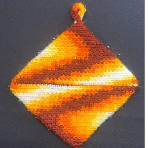 May include: A square, handmade potholder with a loop for hanging. The potholder features a diagonal striped pattern in shades of brown, orange, yellow, and white. The loop is a twisted cord in orange and brown.