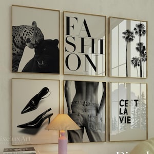 May include: A collection of six framed black and white prints. The prints feature a leopard, the word "FASHION", palm trees, high-heeled shoes, a person's back in jeans, and the phrase "C'est La Vie". A small lamp and books sit on a white cabinet.