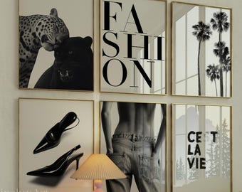 May include: A collection of six framed black and white prints. The prints feature a leopard, the word "FASHION", palm trees, high-heeled shoes, a person's back in jeans, and the phrase "C'est La Vie". A small lamp and books sit on a white cabinet.