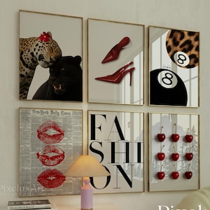 Peut inclure: Ensemble de tirages d'art encadrés représentant un léopard, une panthère noire, des talons hauts rouges, une boule huit porte-bonheur, des lèvres rouges, le mot FASHION et des cerises. Les tirages sont exposés au-dessus d'un meuble blanc avec une lampe.