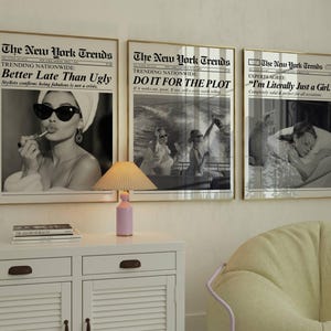 May include: Three framed prints with gold frames, each featuring a black and white image with text. The prints read "Better Late Than Ugly", "Do It For The Plot", and "I'm Literally Just a Girl". A small pink lamp sits on a white cabinet.