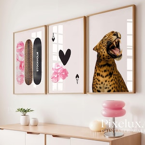 Op de afbeelding: Drie ingelijste kunstafdrukken. Eén toont een skateboard met luipaardprint met de tekst "STOCKHOLM", een andere een zwarte hart en roze bloemen, en de derde een brullende luipaard. De lijsten zijn goudkleurig.