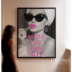 May include: Black and white framed print featuring a woman applying pink lipstick, wearing sunglasses and a towel. The text "BETTER LATE THAN UGLY" is in pink. A stylish wall art piece.