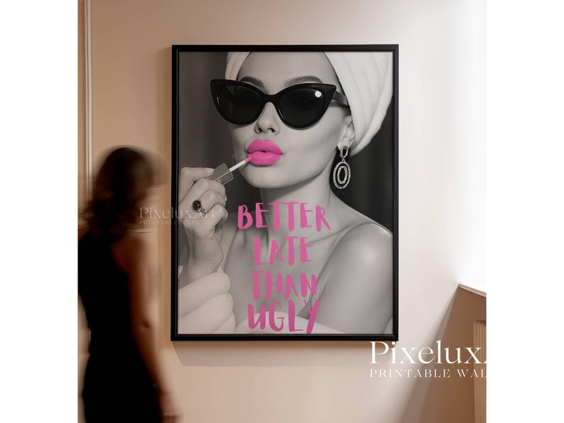May include: Black and white framed print featuring a woman applying pink lipstick, wearing sunglasses and a towel. The text "BETTER LATE THAN UGLY" is in pink. A stylish wall art piece.