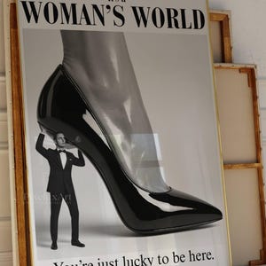May include: A framed poster with the text "WOMAN'S WORLD" at the top. The image features a giant black high-heeled shoe with a man in a tuxedo holding it up. The text "You're just lucky to be here" is at the bottom.