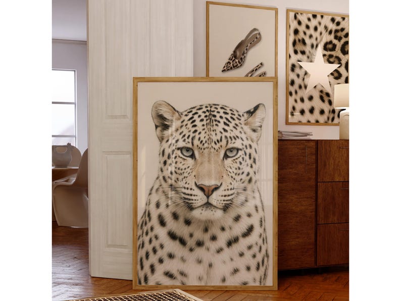 May include: A framed print of a leopard's face with a light beige background. The leopard has black spots and light blue eyes. Two other framed prints are visible in the background, one with a leopard print and a star, and another with a shoe print.