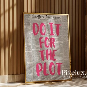Puede incluir: Impresi&oacute;n enmarcada con la frase "DO IT FOR THE PLOT" en letras rosa brillante. El fondo es una impresi&oacute;n de peri&oacute;dico vintage. El marco dorado contrasta con el texto rosa. La impresi&oacute;n est&aacute; apoyada contra una pared de madera.