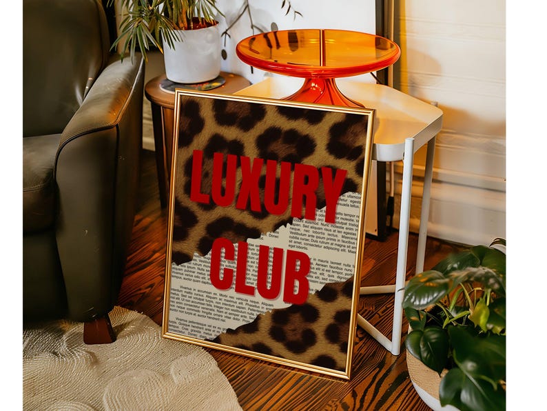 May include: A framed art print with a gold border. The print features a leopard print design with the words "LUXURY CLUB" in bold red letters. The background is a torn newspaper. The artwork is displayed in a room with a green sofa and a small side table.