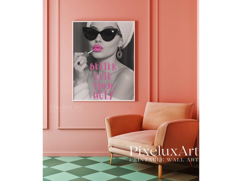 May include: A framed black and white print featuring a woman applying lipstick, wearing sunglasses and a head wrap. The pink text on the print reads "BETTER LATE THAN UGLY". The print hangs on a pink wall above a peach armchair.