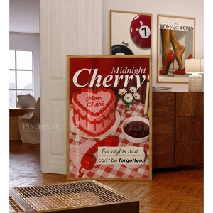 May include: A framed art print featuring a heart-shaped cake with the words "Midnight Cherry" and "Mon Ch&eacute;ri." The print also includes a red telephone and the text "For nights that can't be forgotten." Other framed prints are visible.