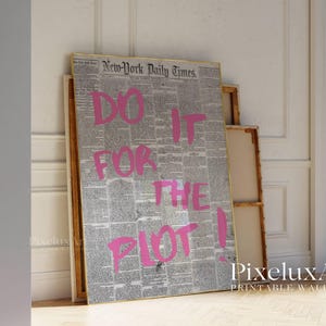 May include: A framed print featuring a vintage newspaper background with the text "DO IT FOR THE PLOT!" in bright pink. The artwork leans against a wall, showcasing a bold statement piece for home decor.
