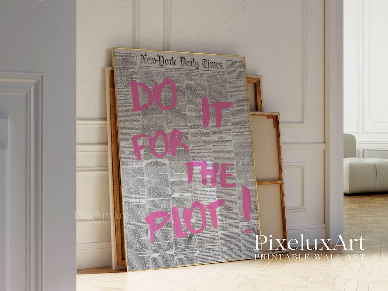 May include: A framed print featuring a vintage newspaper background with the text "DO IT FOR THE PLOT!" in bright pink. The artwork leans against a wall, showcasing a bold statement piece for home decor.
