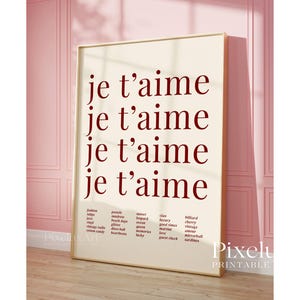 May include: A framed print with the words "je t'aime" repeated four times in a burgundy font. Below the text are lists of words. The print is displayed against a pink wall.