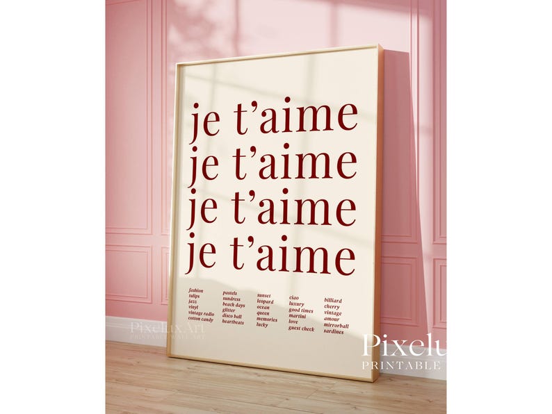 May include: A framed print with the words "je t'aime" repeated four times in a burgundy font. Below the text are lists of words. The print is displayed against a pink wall.