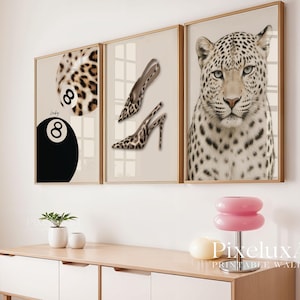 May include: Three framed wall art prints. One features a leopard print 8-ball, another shows leopard print high heels, and the third is a close-up of a leopard's face. The frames are gold-toned.