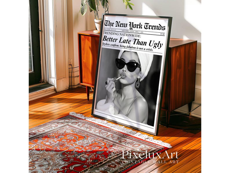 May include: Black and white framed print featuring a woman applying lipstick, wearing sunglasses and a towel on her head. The print is styled as a newspaper front page with the headline "Better Late Than Ugly."