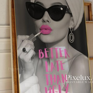 May include: Black and white print of a woman applying pink lipstick, wearing sunglasses and earrings. The text "BETTER LATE THAN UGLY" is in pink. The artwork is framed in a gold-colored frame. Printable wall art.