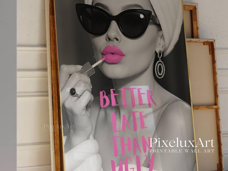 May include: Black and white print of a woman applying pink lipstick, wearing sunglasses and earrings. The text "BETTER LATE THAN UGLY" is in pink. The artwork is framed in a gold-colored frame. Printable wall art.
