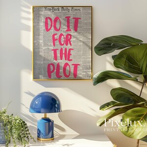 Puede incluir: Una impresi&oacute;n enmarcada con el texto "DO IT FOR THE PLOT" en rosa brillante sobre un fondo de peri&oacute;dico. Una l&aacute;mpara azul con base dorada se encuentra sobre una superficie blanca. A la derecha hay una gran planta verde.