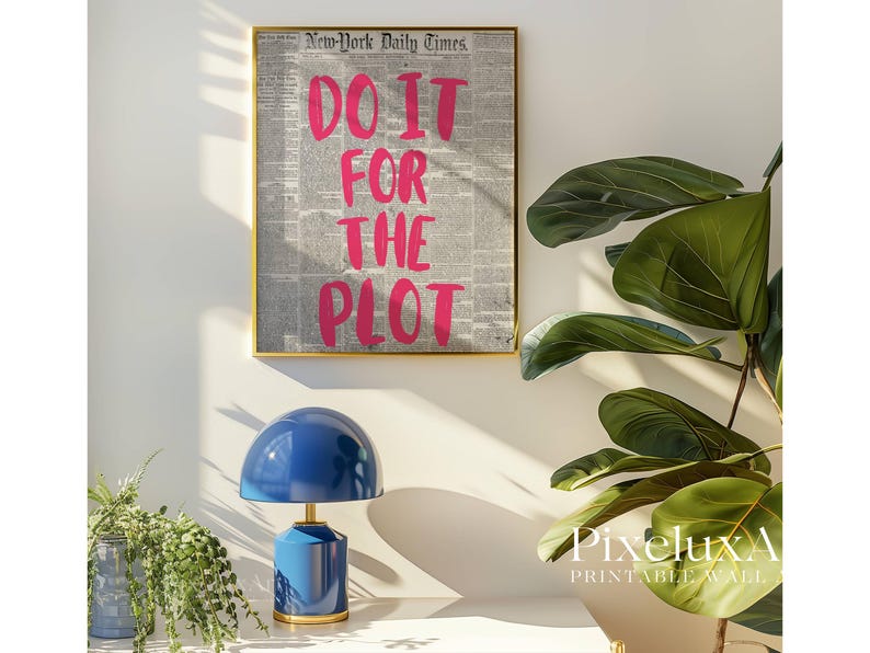 Puede incluir: Una impresi&oacute;n enmarcada con el texto "DO IT FOR THE PLOT" en rosa brillante sobre un fondo de peri&oacute;dico. Una l&aacute;mpara azul con base dorada se encuentra sobre una superficie blanca. A la derecha hay una gran planta verde.
