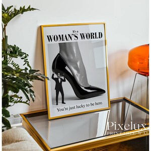 May include: Framed art print with a black and white image of a high-heeled shoe supported by a tiny man in a suit. The text reads "It's a WOMAN'S WORLD" and "You're just lucky to be here."