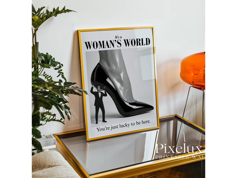 May include: Framed art print with a black and white image of a high-heeled shoe supported by a tiny man in a suit. The text reads "It's a WOMAN'S WORLD" and "You're just lucky to be here."