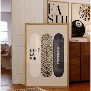 May include: Framed wall art featuring three skateboard designs. One is white with "C'est la Vie" text, another has a leopard print, and the third is black with "Stockholm" text. Additional framed art pieces with "FASH" and a leopard print design are visible.