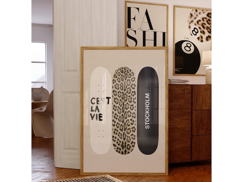 May include: Framed wall art featuring three skateboard designs. One is white with "C'est la Vie" text, another has a leopard print, and the third is black with "Stockholm" text. Additional framed art pieces with "FASH" and a leopard print design are visible.