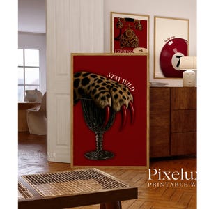 May include: A framed print with a red background features a leopard paw with long red claws emerging from a dark glass. The words "STAY WILD" are printed in white. Other framed prints are visible.
