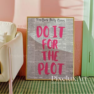 Puede incluir: Una impresi&oacute;n enmarcada con el texto "DO IT FOR THE PLOT" en rosa brillante sobre un fondo de peri&oacute;dico vintage. La impresi&oacute;n est&aacute; en un marco dorado y se muestra contra una pared rosa.